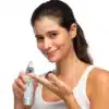 Nainen käyttää Repechage-ihonhoitotuotetta kasvoilleen, hymyilee ja pitää pulloa ja voidetta käsissään.