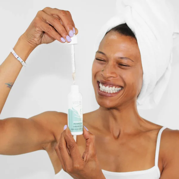Nainen pyyhkeellä päähän kiedottuna käyttää pipettiä levittääkseen Repechage ihonhoitotuotetta pullosta, hymyillen iloisesti.
